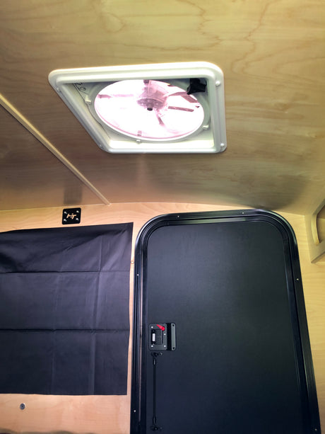 Inside an rv rental: light wood interior with a ceiling fan, black privacy curtain, and door, ready for your next adventure.