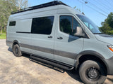 This grey camper van, equipped with a roof rack and rugged side steps, is ready for your RV rental journey.