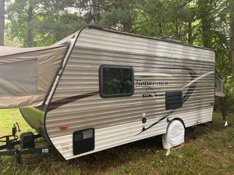 A beige pop-up hybrid travel trailer, an ideal rv rental for outdoor camping, is set up in a wooded site.