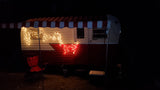 Cozy vintage RV rental at night with festive string lights and awning, perfect for glamping.