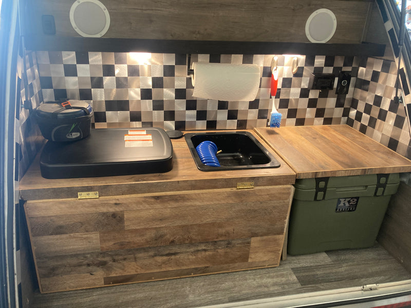 Functional **RV rental** kitchen featuring a stove, sink, cooler, and checkerboard backsplash. — photo 8