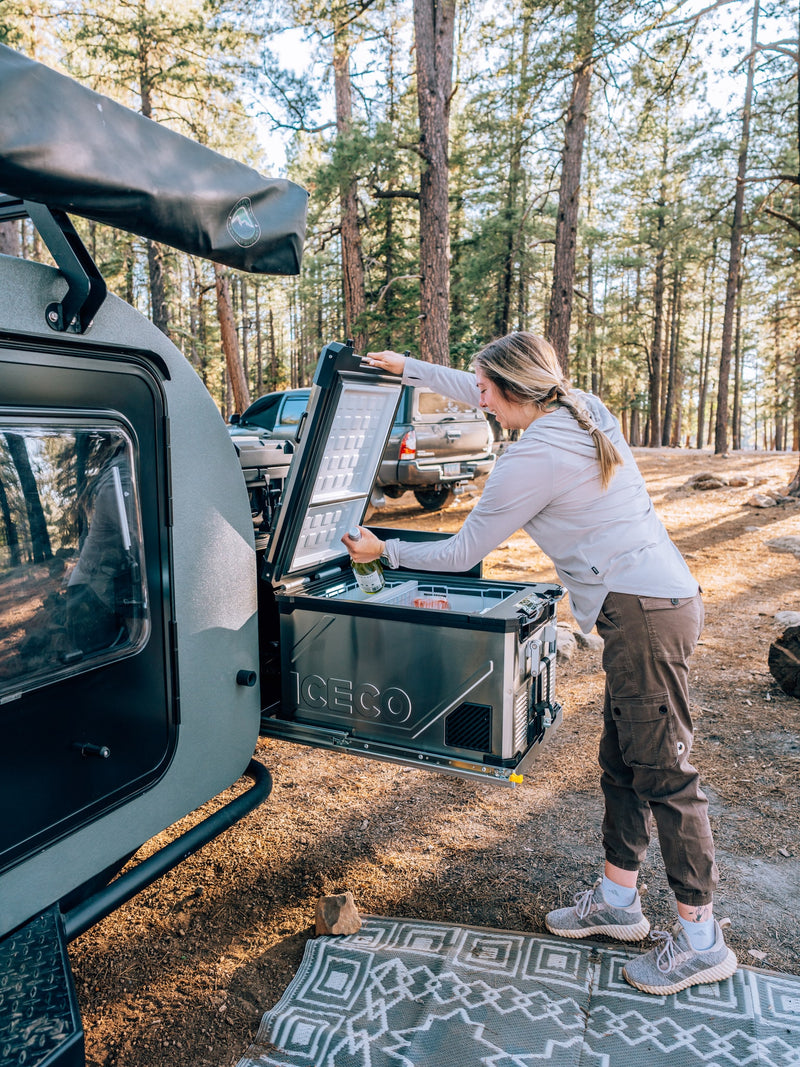Woman restocking ICECO fridge on an RV rental teardrop camper in a sunny pine forest. Ready for adventure! — photo 16