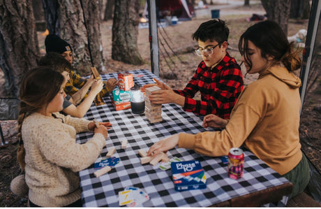 Friends and family enjoy games like Jenga and cards at an RV rental campsite picnic table.