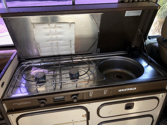This Westfalia RV rental features a compact kitchen with a two-burner stove and sink, perfect for camping.