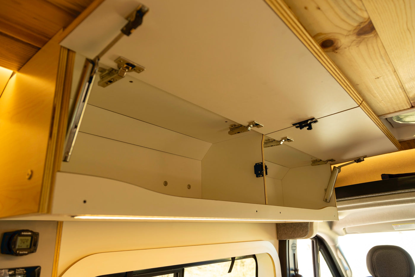 View of open overhead storage cabinets with built-in LED lighting in an RV rental interior, featuring light cabinetry and a wood ceiling. — photo 17