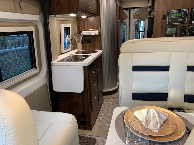 RV rental: Interior shows compact kitchen with sink/stovetop, and dining booth with place setting. — photo 2