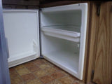 An open, empty compact mini-fridge in an RV rental, showing shelves. Perfect for your travel snacks.