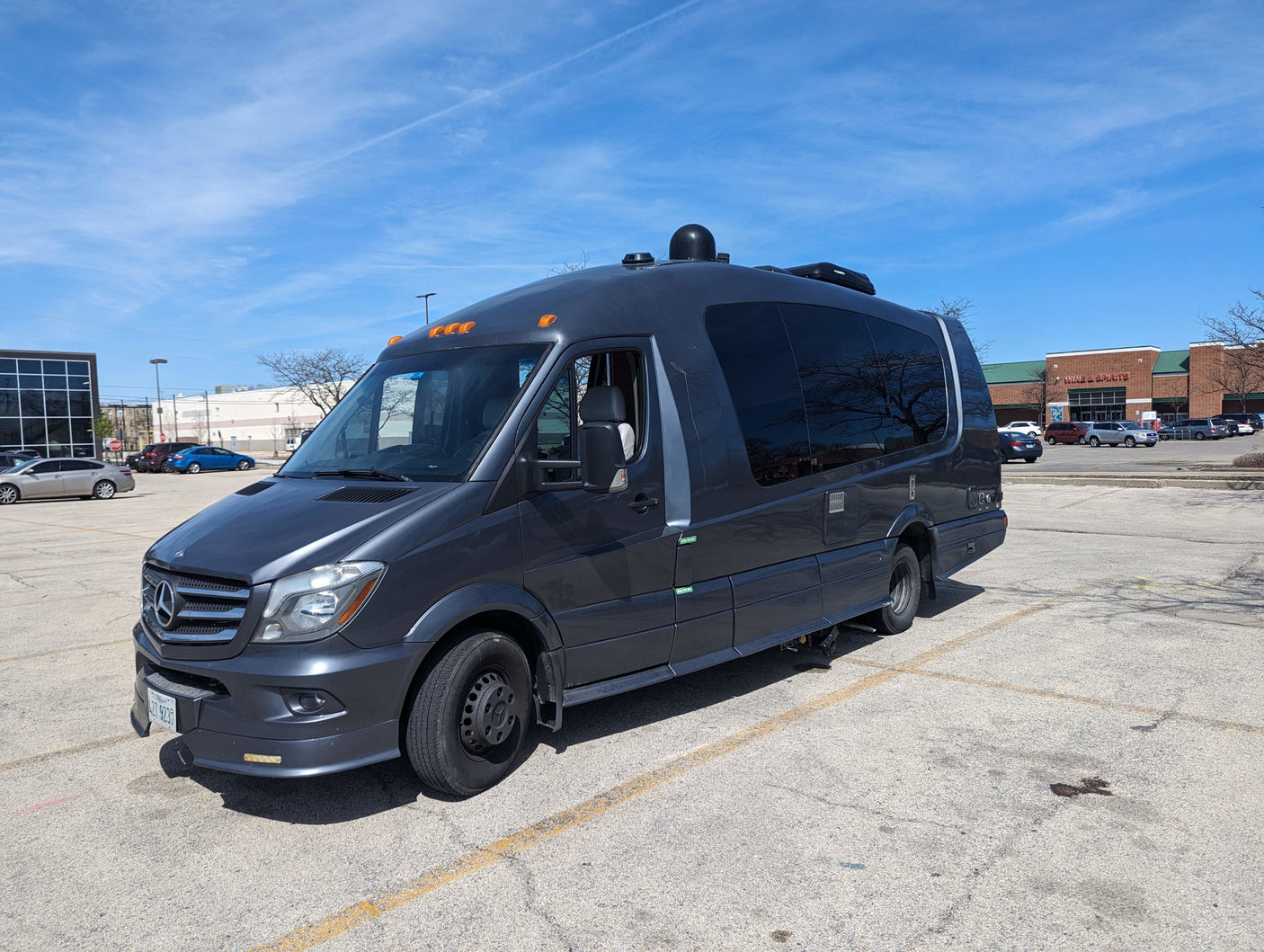 A dark gray Mercedes-Benz Sprinter van, customized as an RV rental, parked in a sunny lot. Note tinted windows & roof equipment.