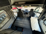 RV rental: Camper van interior with a flat black quilted bed, front seats, and gray fabric walls.