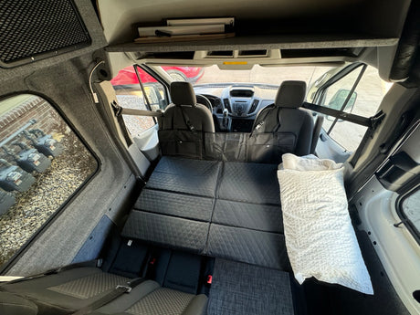 RV rental: Camper van interior with a flat black quilted bed, front seats, and gray fabric walls.