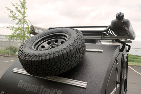 Off-road RV rental trailer featuring a mounted spare tire, roof rack, and water tank. Ready for adventure.