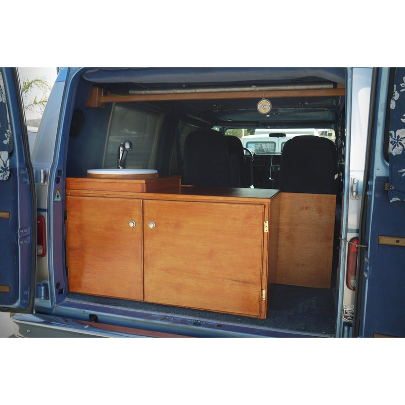 Inside an RV rental, a custom-built camper van features wooden cabinets, a sink, and blue carpet flooring. — photo 7