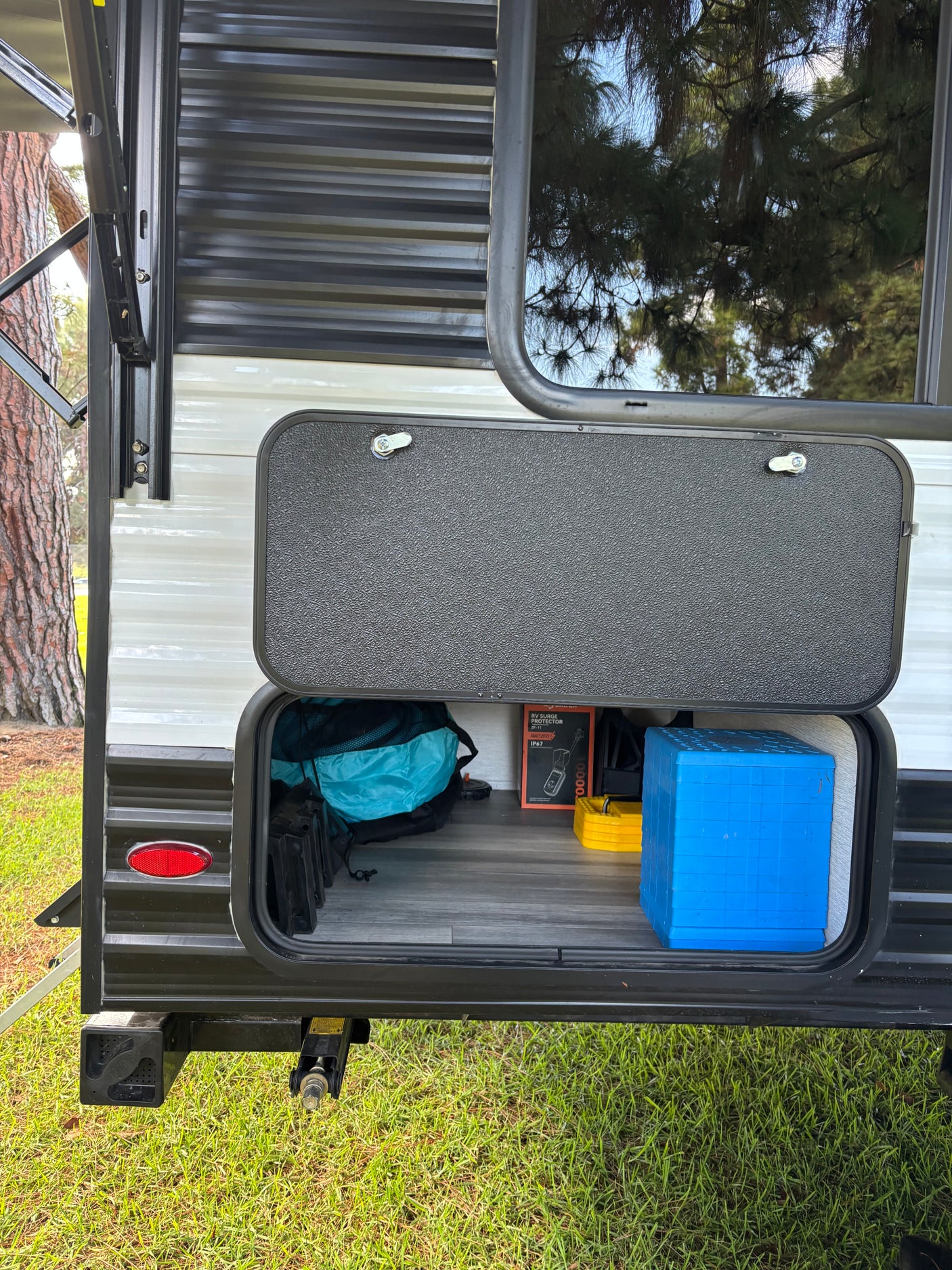 RV rental: Open exterior storage compartment revealing essential camping gear: surge protector, leveling blocks, blue step.