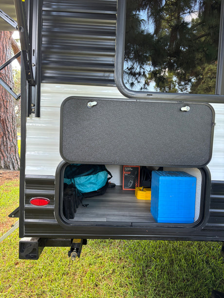 RV rental: Open exterior storage compartment revealing essential camping gear: surge protector, leveling blocks, blue step.