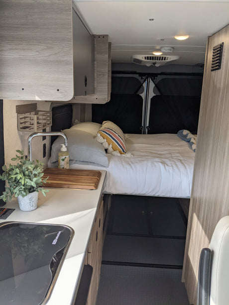 Cozy RV rental interior showing a compact kitchen with sink and stovetop, and a comfortable bed. Perfect for mobile adventures.