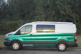 Side view of a green & white Hawaii Surf Campers RV rental van with "DO NOT CLIMB ON ROOF" visible, reflecting the sunset.