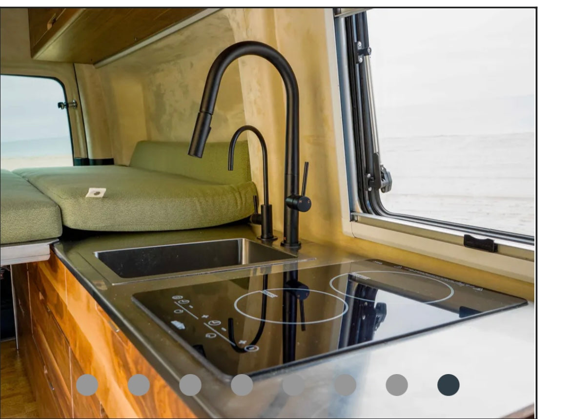 RV rental: Modern camper kitchen with sink, induction cooktop, green bed, and window offering a bright beach view.