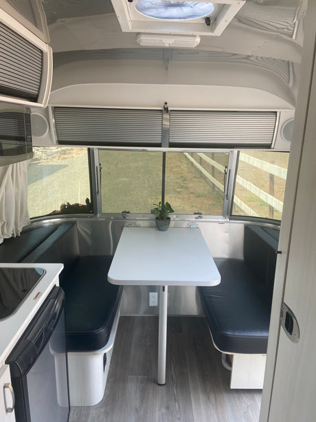 Modern RV rental interior: A bright dinette with black benches, overhead storage, and kitchen area for comfortable travel.