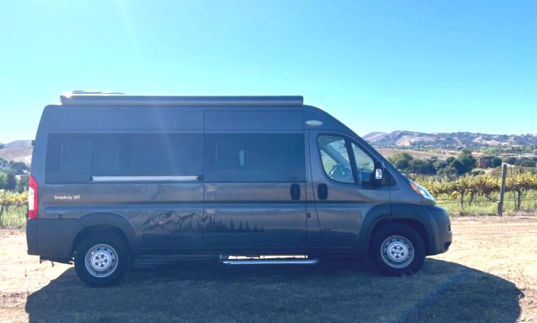 Scenic RV rental adventure: Dark gray camper van parked at a vineyard with hills and clear blue sky.|Explore this cozy rv rental camper van interior: compact kitchen with sink
