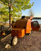 Unique wooden teardrop camper parked by a lake, ideal for an RV rental adventure. Enjoy lakeside camping.