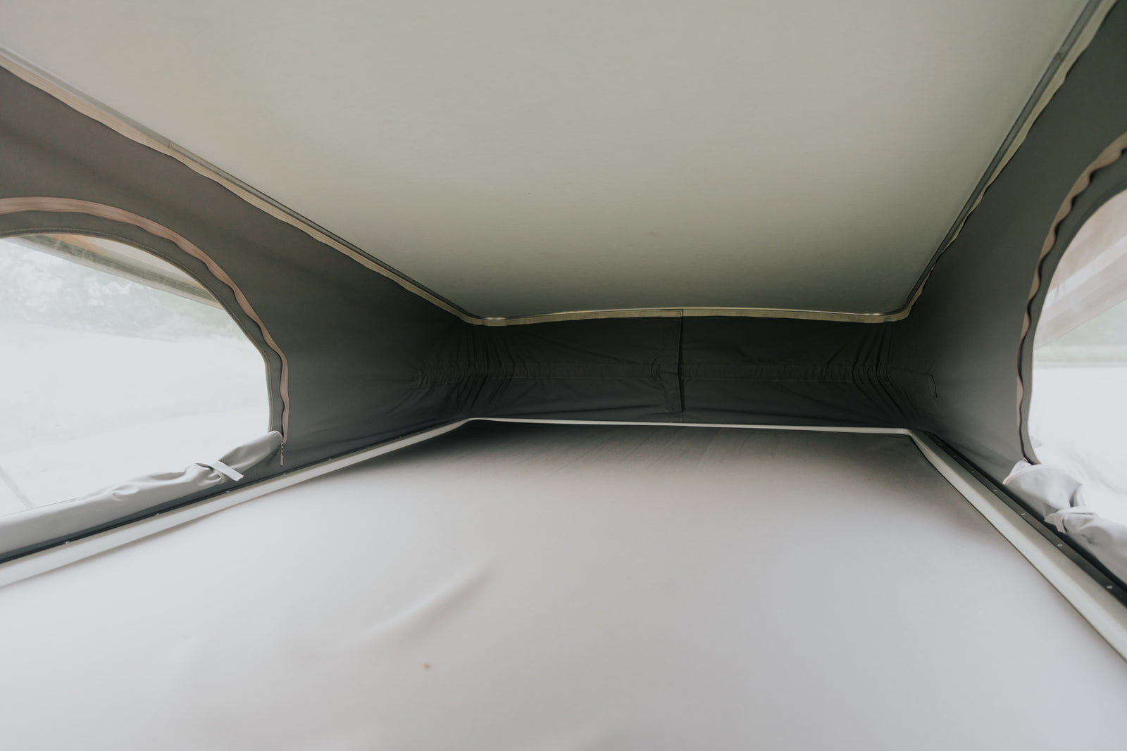 Inside a spacious pop-top RV rental with a comfortable raised bed, showing the tent walls and clear windows.