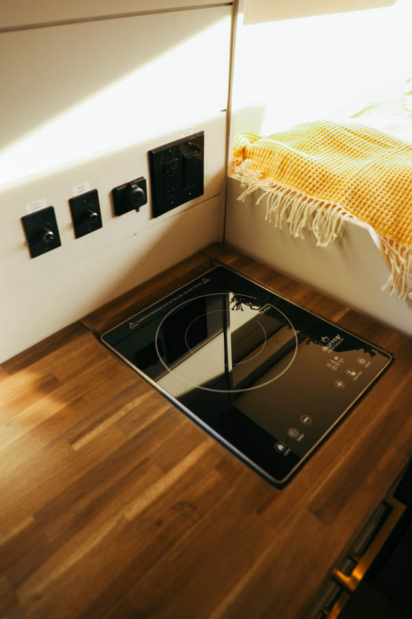 RV rental interior: A modern kitchen area with an induction cooktop, wooden counter, and wall-mounted controls.