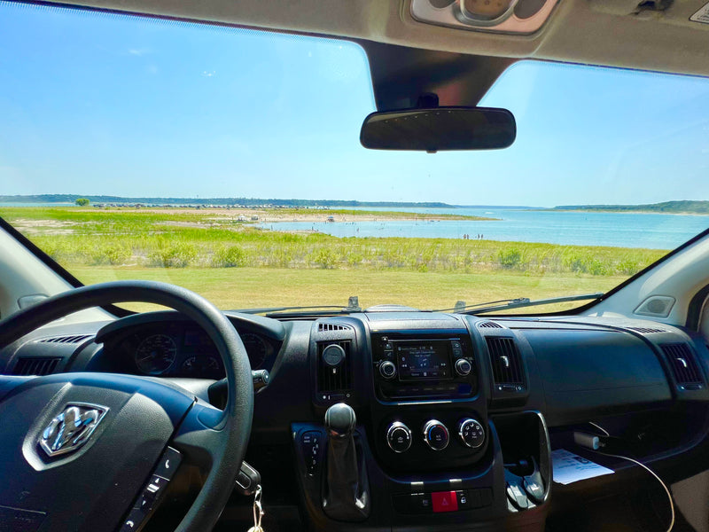 Inside an RV rental van, enjoying a scenic lake view from the dashboard. People and cars are visible by the grassy shore. — photo 12