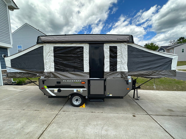 A gray and white Flagstaff MAC pop-up camper is set up on a driveway. Perfect for an RV rental!