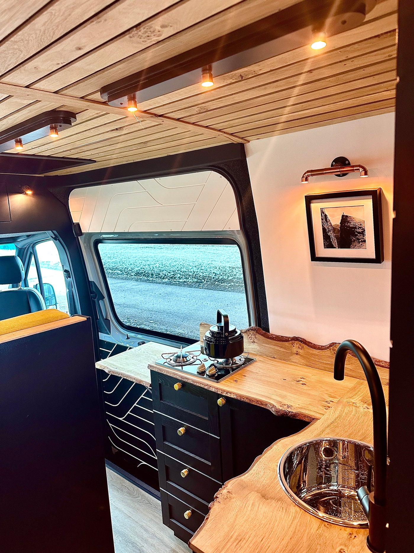 A modern rv rental interior showcasing a beautiful live-edge wood kitchen, sink, stove, and cozy lighting. — photo 7