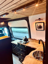 A modern rv rental interior showcasing a beautiful live-edge wood kitchen, sink, stove, and cozy lighting.