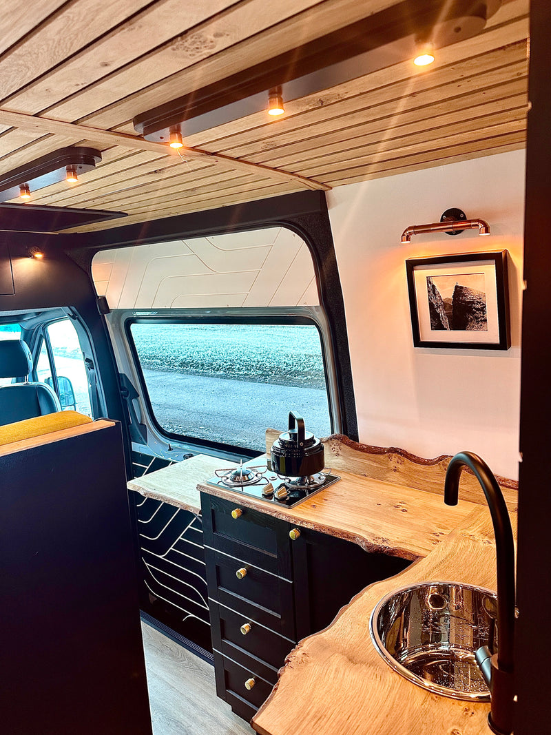 A modern rv rental interior showcasing a beautiful live-edge wood kitchen, sink, stove, and cozy lighting. — photo 7