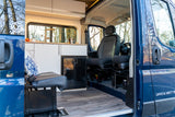 Spacious rv rental camper van interior. Features compact kitchen, bench seat, and front cabin area with driver's seat.