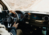 Driving an RV rental: View from driver's seat. Hands on Mercedes wheel, dashboard, and infotainment system with music.