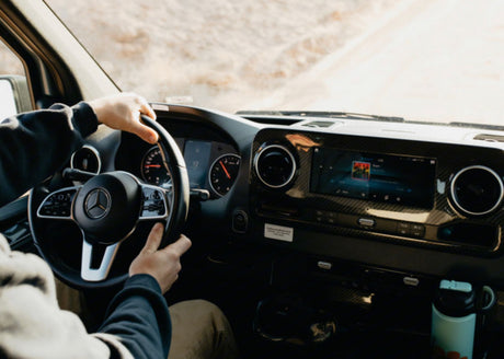 Driving an RV rental: View from driver's seat. Hands on Mercedes wheel, dashboard, and infotainment system with music.