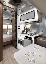 Explore this Airstream RV rental interior, featuring a compact kitchen, dining area with games, and a cozy bedroom.
