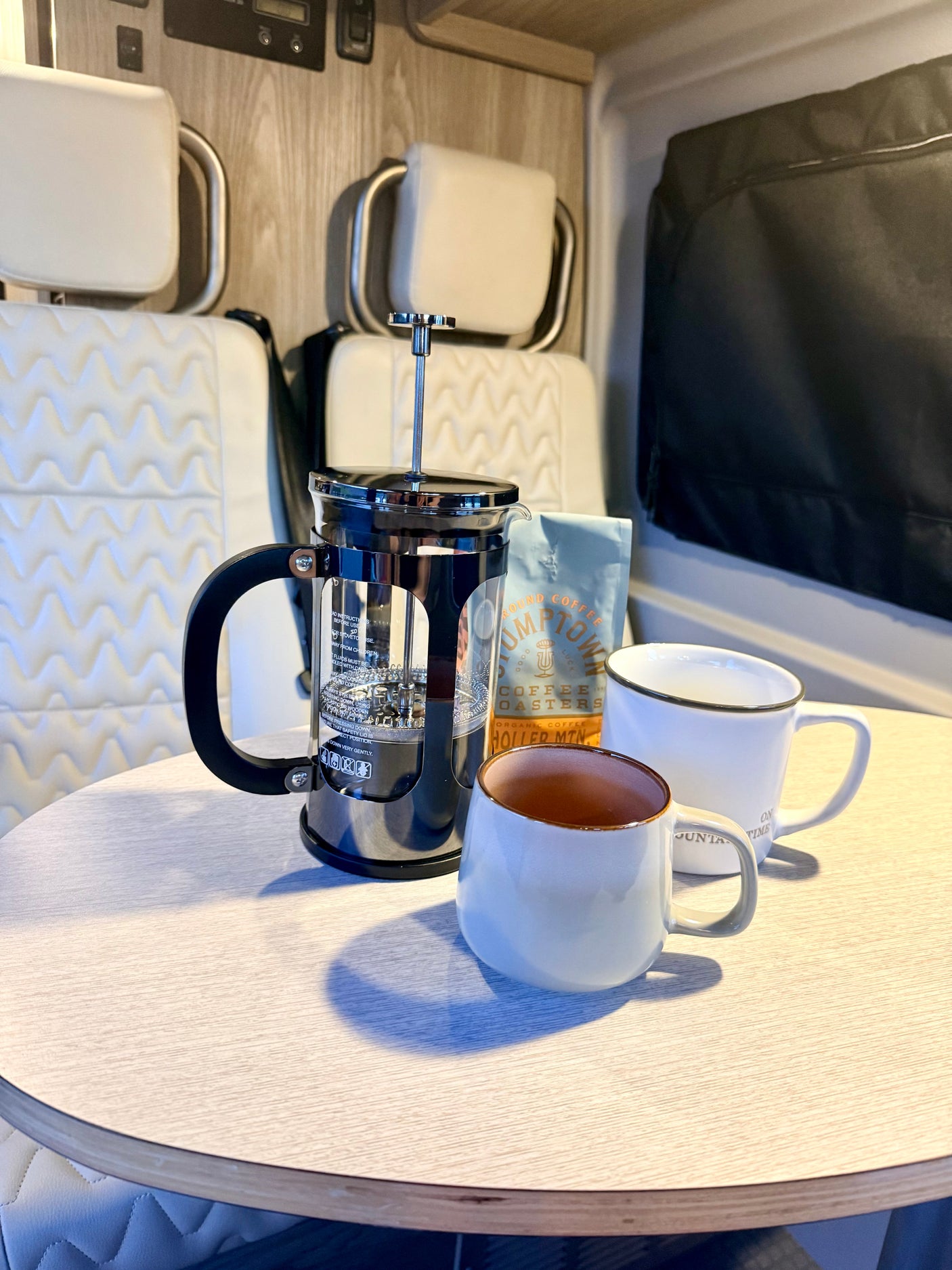 Morning coffee in an RV rental: French press, Stumptown coffee, and two mugs on a table, with comfortable seating.