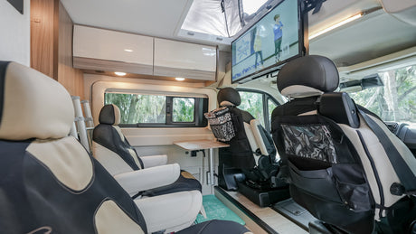 Inside a modern RV rental, featuring comfortable swivel seats, a ceiling-mounted TV, and pull-out table for travelers.