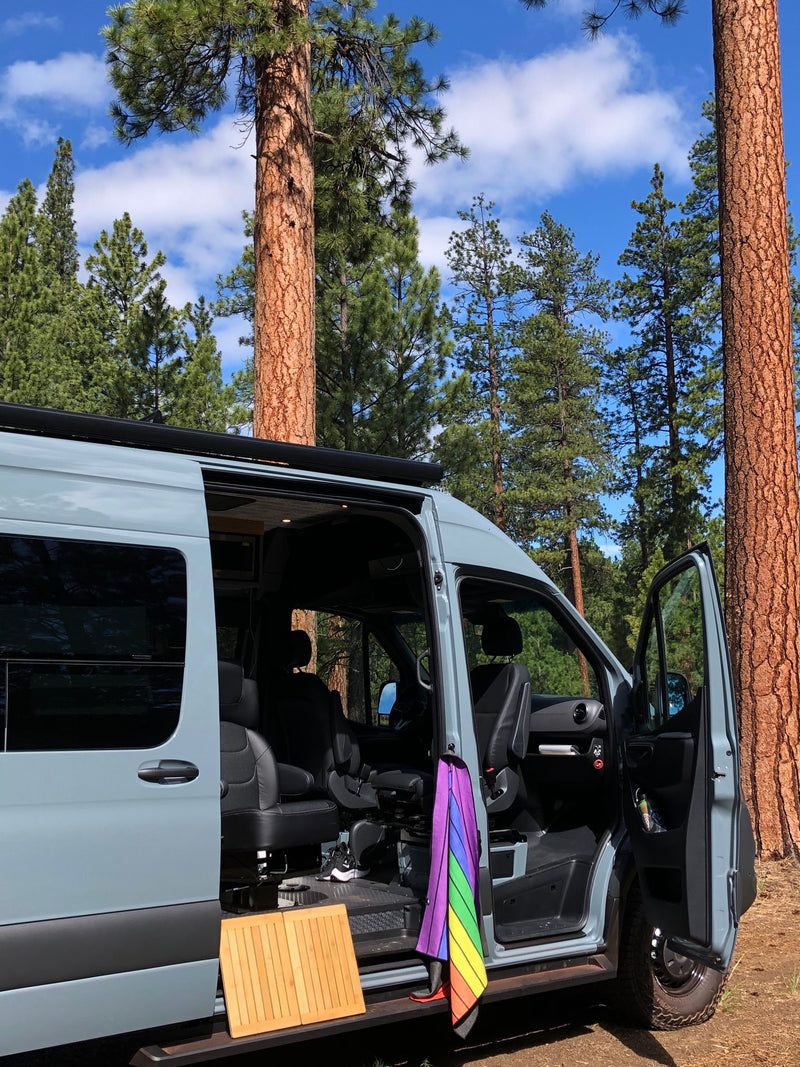 Light gray camper van RV rental parked in a sunny forest, its passenger door open revealing a rainbow umbrella. — photo 20
