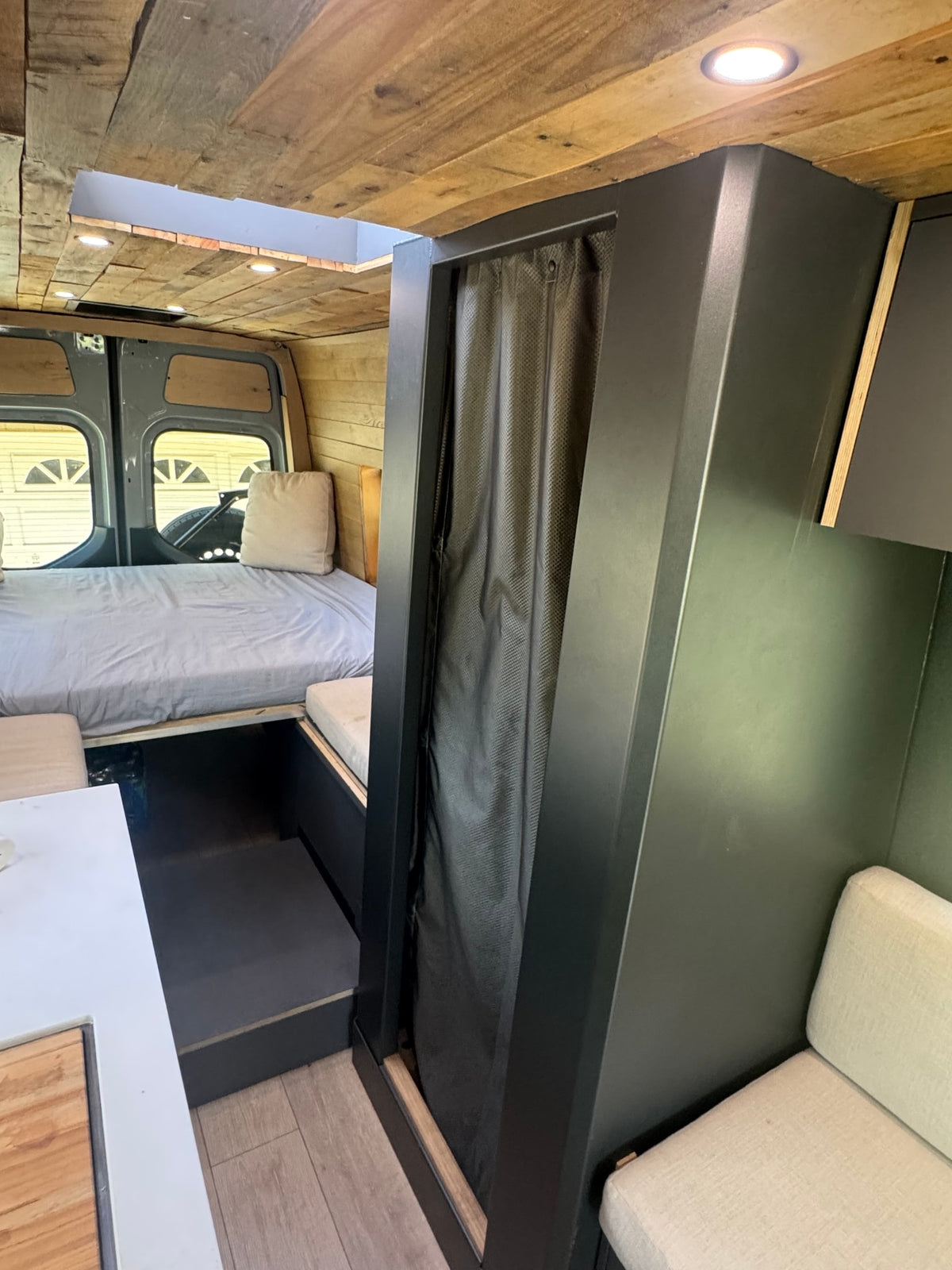 Cozy rv rental interior featuring a bed, woody ceiling, compact living area with kitchen space, and a dark privacy unit. — photo 17