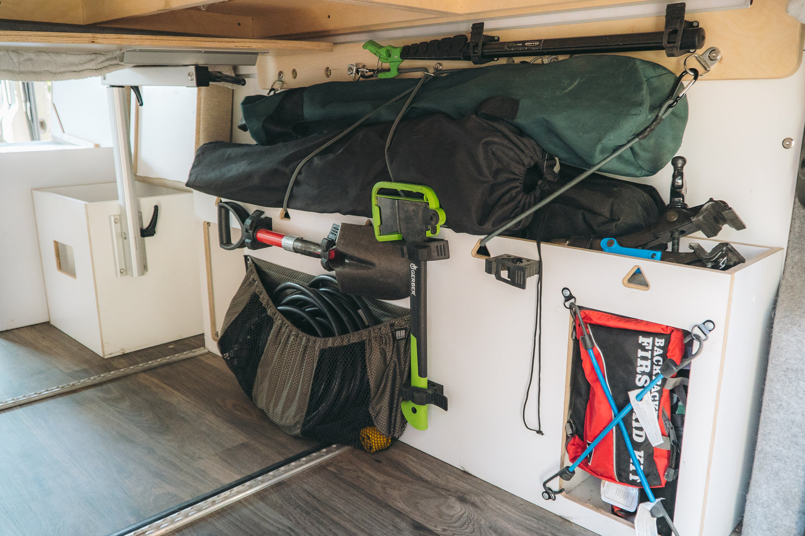RV rental storage: Organized camper cargo holds a shovel, Gerber tool, gear bags, coiled hoses, and a first aid kit.
