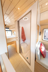 Modern RV rental interior: a compact shower/toilet, with a bed in the background & a cozy seating area on the right.