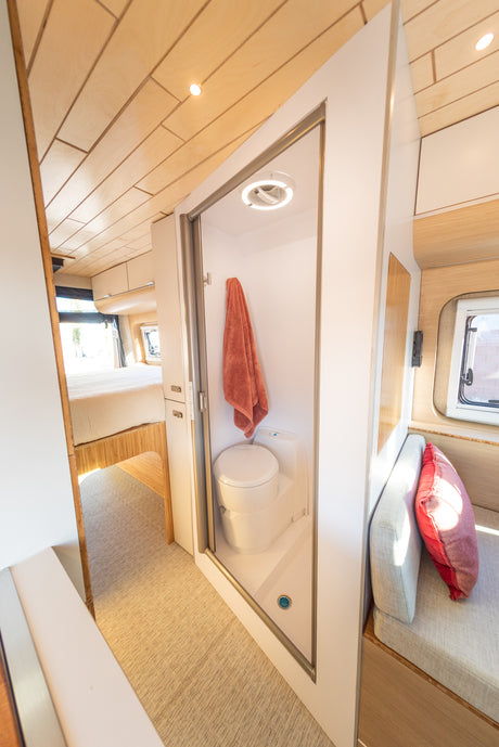 Modern RV rental interior: a compact shower/toilet, with a bed in the background & a cozy seating area on the right.