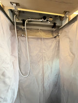 Inside an RV rental, a compact fabric shower stall with a hanging shower head and hose, designed for travel.
