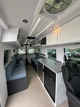 Modern RV rental interior: bright white walls, blue seating, and a fully equipped kitchen with appliances.