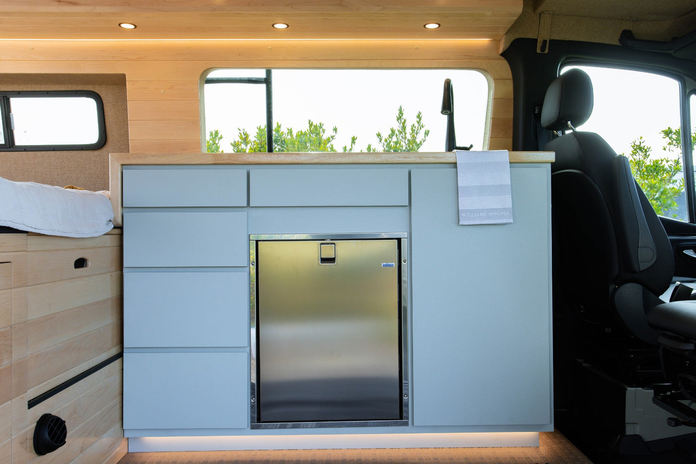 This rv rental features a sleek light blue kitchen with built-in fridge, sink, and a comfy bed.
