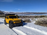 Bright yellow Jeep Rubicon on a snowy trail beside a reflective lake with mountains.