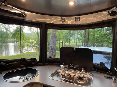 RV rental kitchen: coffee brewing with a scenic lake & forest view from the camper window!