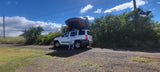 White SUV with rooftop tent (RV rental) & ladder on a dirt road. Ready for camping adventures under blue skies.