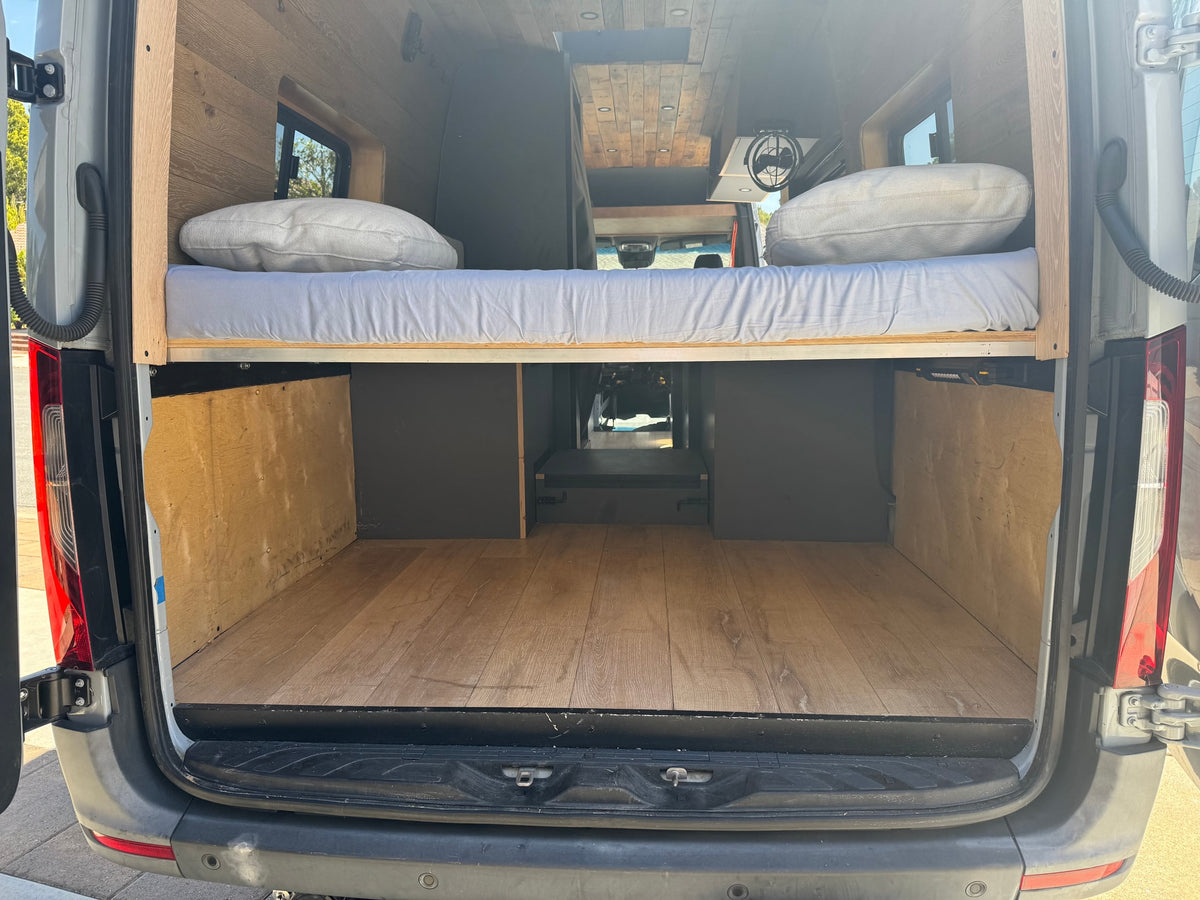 Inside an RV rental: a cozy van conversion with elevated wooden bed, mattress, pillows, and spacious cargo storage. — photo 9