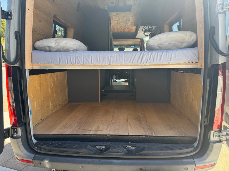 Inside an RV rental: a cozy van conversion with elevated wooden bed, mattress, pillows, and spacious cargo storage. — photo 9